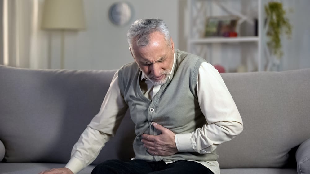Man experiencing abdominal pain on couch, Covidien hernia mesh complications and revision surgery symptoms